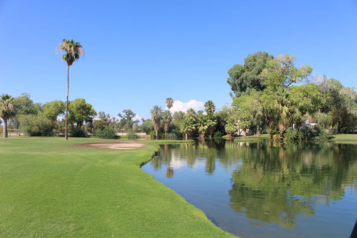 A picturesque golf course with a tranquil pond and lush greenery under a clear blue sky.