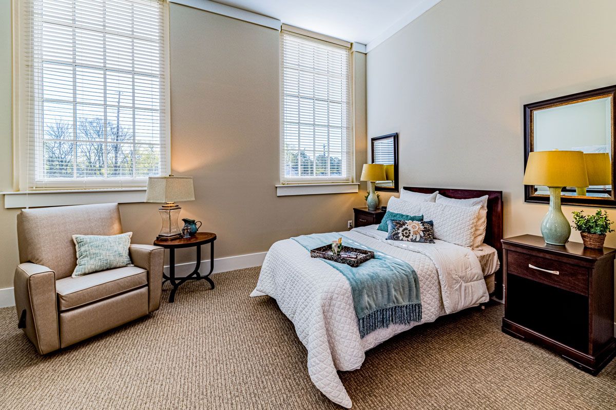 A cozy and well-decorated bedroom with a large window, featuring a bed, armchair, and stylish decor.