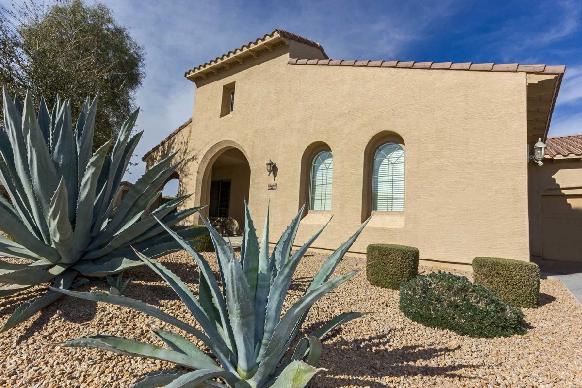 A house with a desert landscape featuring succulents under a clear blue sky.