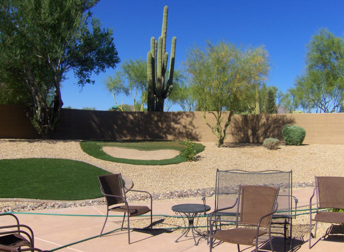 A relaxing patio setup with chairs and a table overlooking a desert landscape featuring cacti and trees under a clear blue sky.