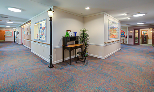 A hallway with a small desk and chair, featuring artwork on the walls and a decorative lamp post.