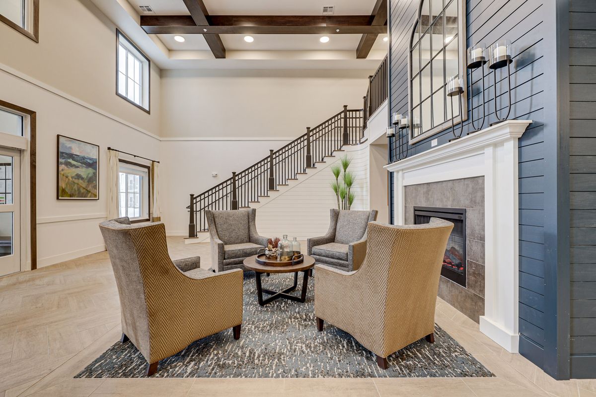 A modern living room with armchairs arranged around a coffee table, featuring a fireplace and a staircase in the background.