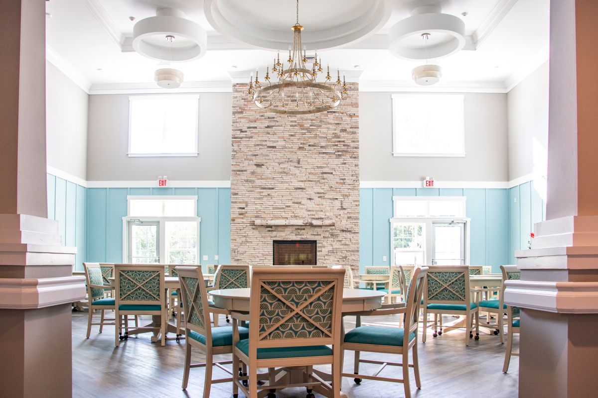 A spacious dining room featuring a stone fireplace, elegant chandelier, and stylish wooden furniture in a bright, light-filled space.