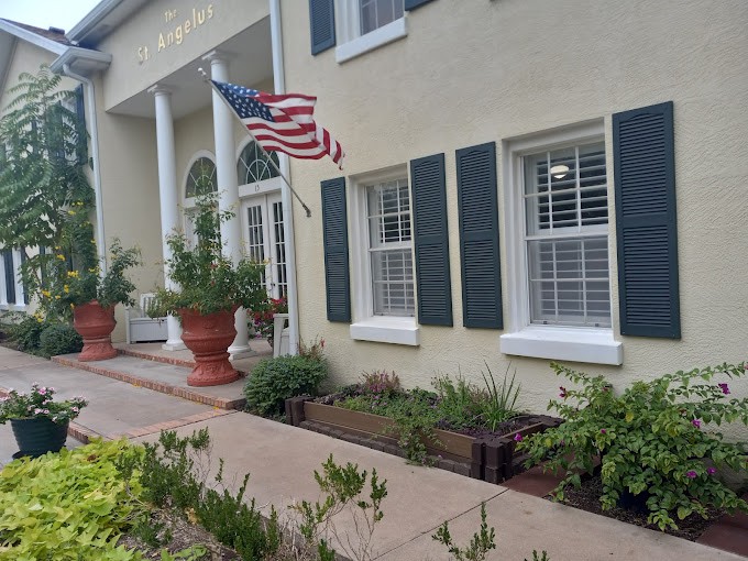 A building with white columns and an American flag, surrounded by potted plants and landscaping.