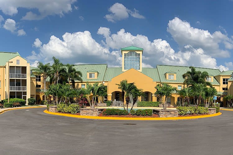 A tropical resort building with palm trees under a blue sky with clouds.