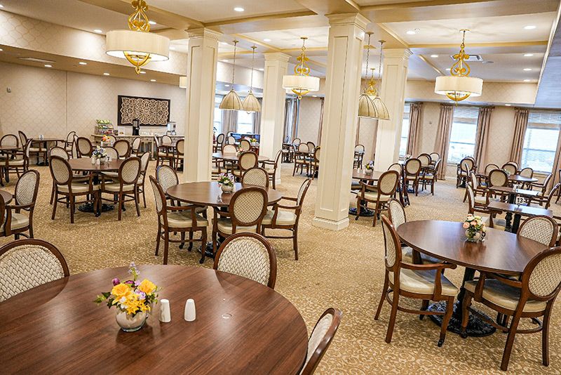 A spacious and elegantly designed dining room with multiple tables and chairs, featuring chandeliers and a carpeted floor.