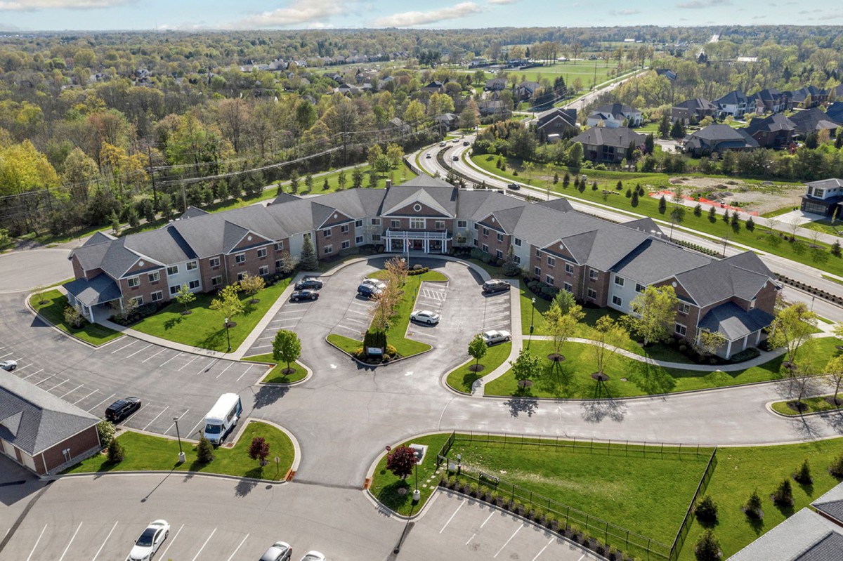 Aerial view of a large residential building with a surrounding parking lot and extensive greenery.
