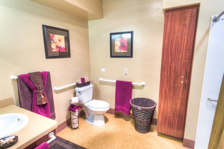 A neatly decorated bathroom featuring vibrant purple towels, wall art, and a wicker wastebasket.
