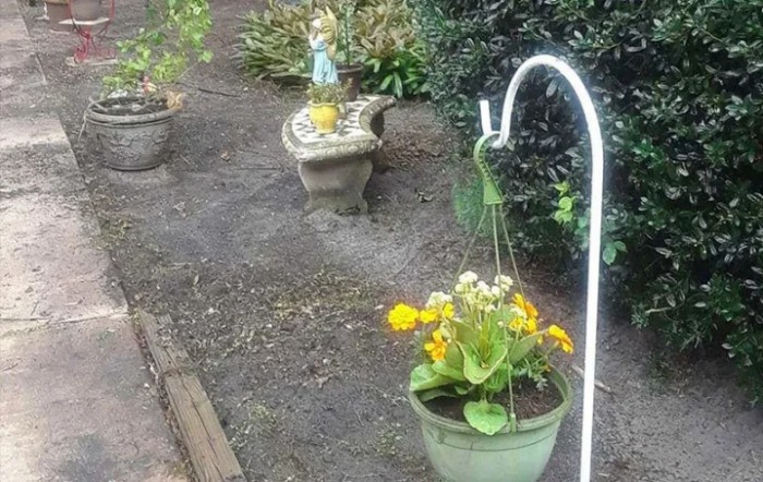 A garden scene featuring a hanging planter with vibrant yellow flowers and decorative elements along a pathway.
