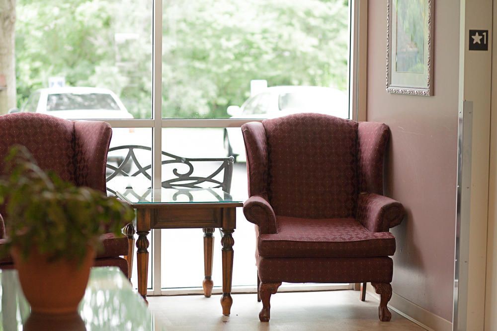 Cozy chairs and a small table by a large window in a sunlit living room.