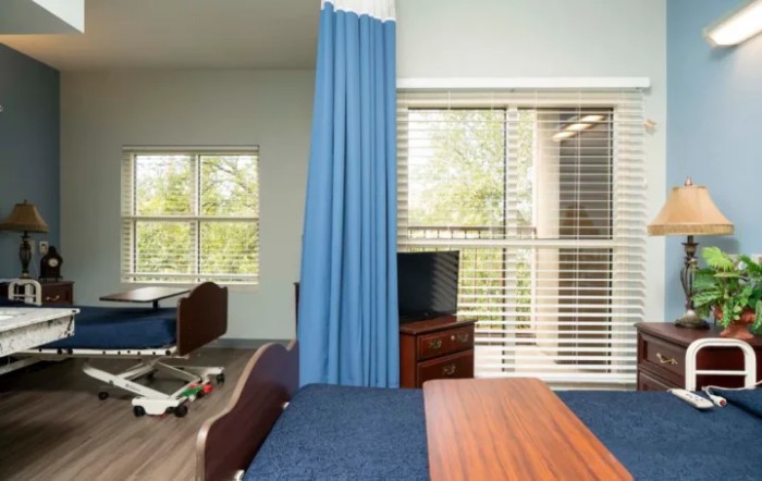 A hospital room featuring a patient bed, curtain divider, and a window with blinds.