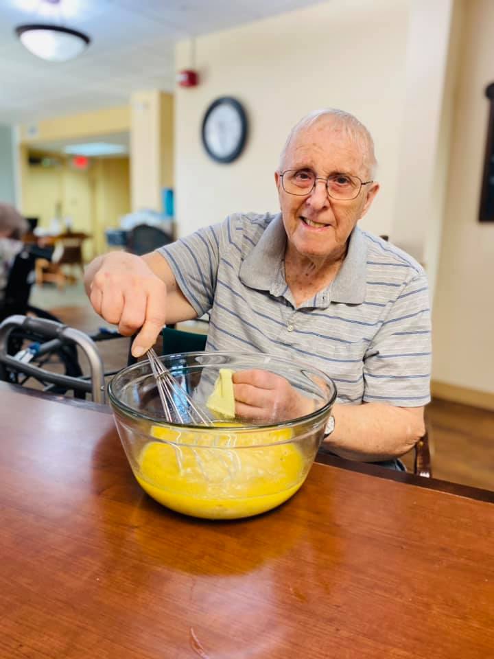 An elderly man happily mixing ingredients in a bowl.