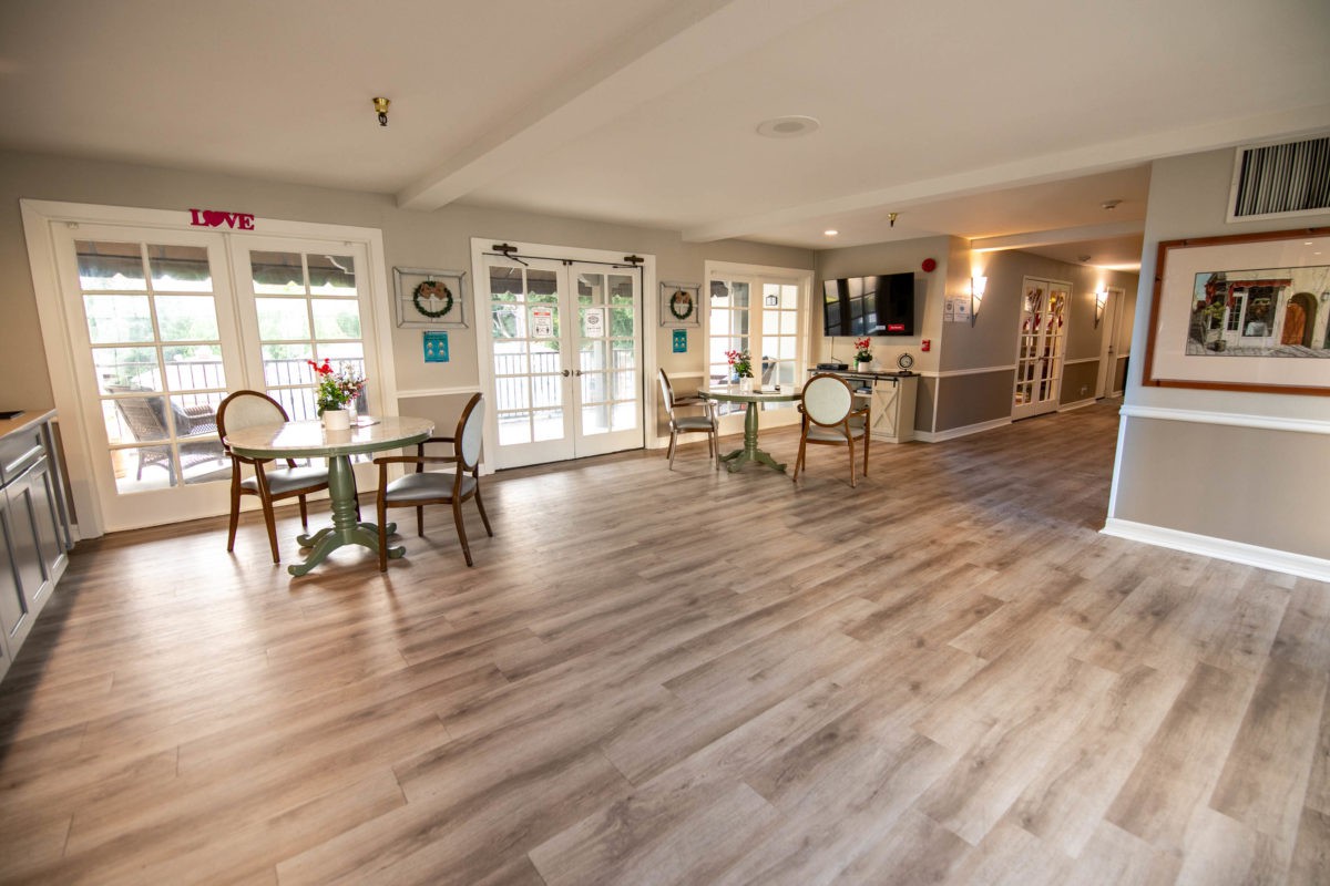 A spacious and well-lit dining area with wood flooring, featuring tables and chairs near large windows.