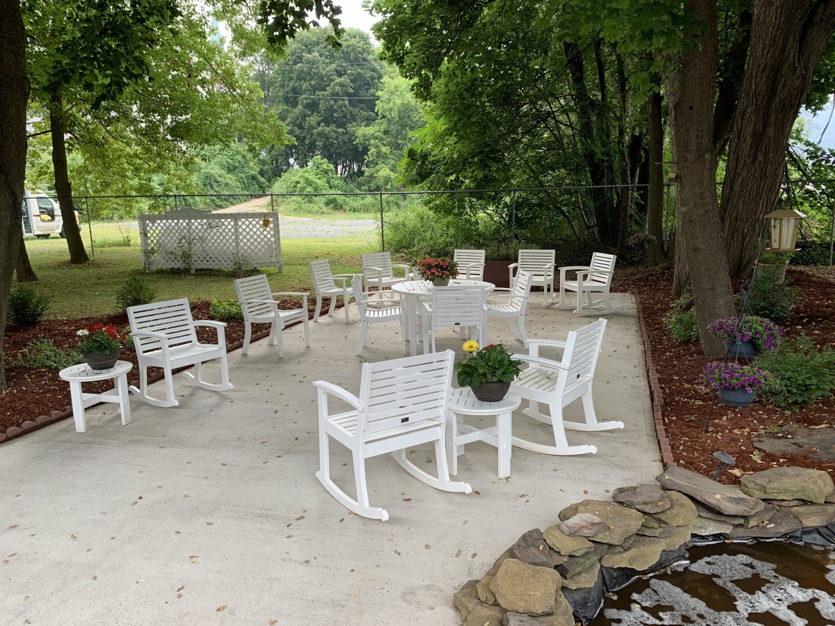 An outdoor seating area featuring white rocking chairs on a patio surrounded by trees.