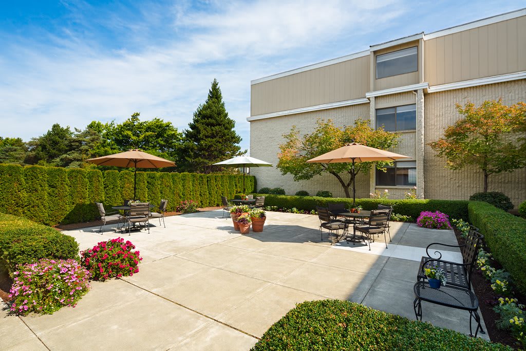 A well-maintained outdoor patio area with tables, chairs, and umbrellas, surrounded by greenery.