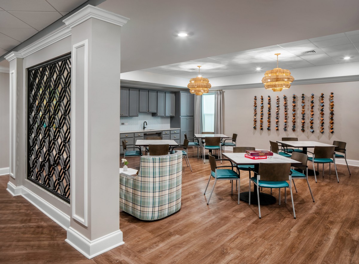 A modern dining area with a kitchenette, featuring wooden floors and stylish chandeliers.