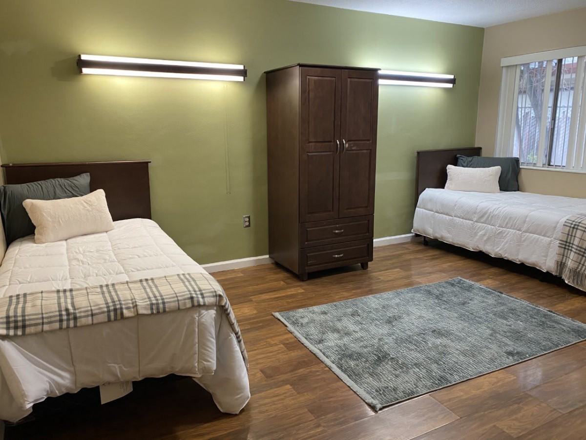 A bedroom with two single beds, a central wardrobe, and a decorative area rug on a wooden floor.