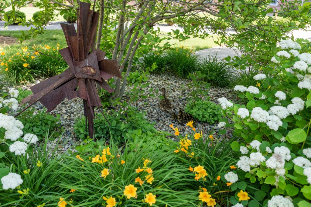 A serene garden scene with flowers, a duck, and a metal sculpture.