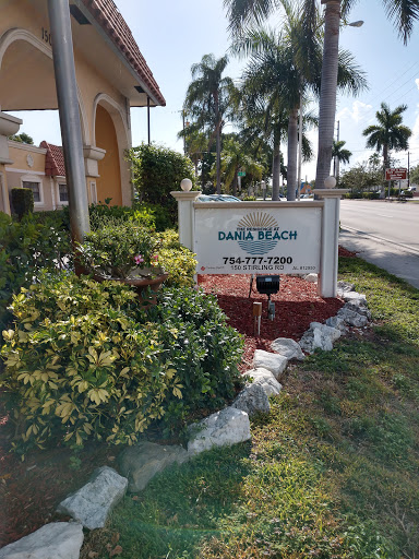 A welcoming sign for a residential community, surrounded by lush greenery and palm trees.