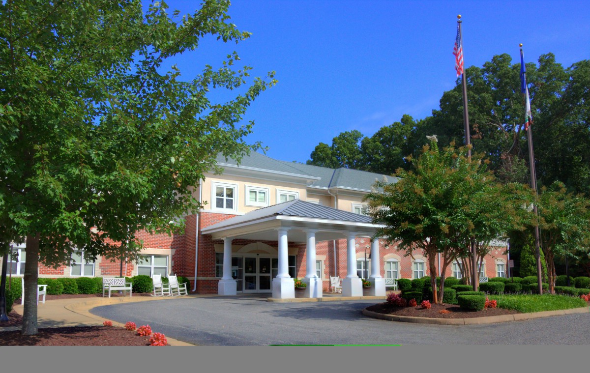 A large building with a prominent entrance, surrounded by trees and displaying a flag.