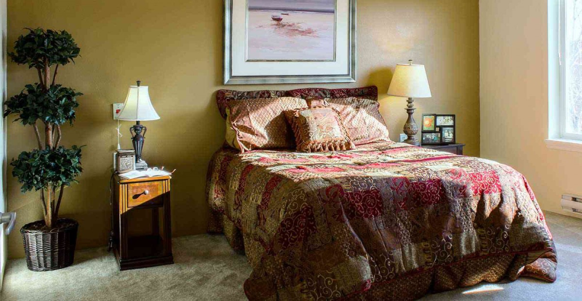 A cozy bedroom with a neatly made bed, two lamps on nightstands, and a painting above the headboard.