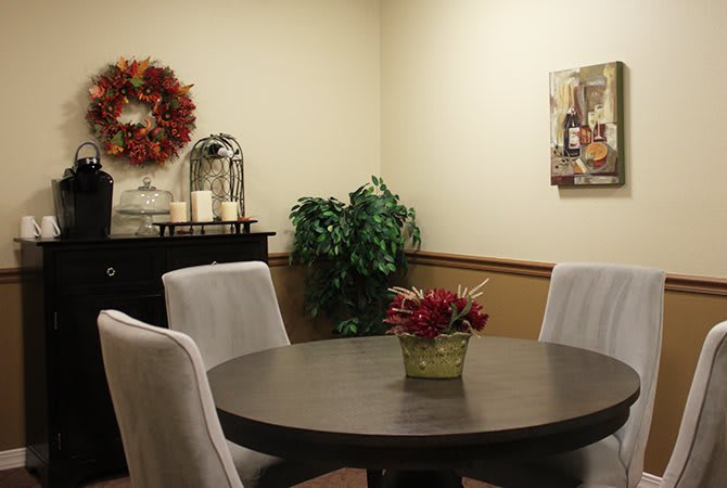 A cozy dining room with a round table surrounded by upholstered chairs, decorated with a centerpiece and seasonal wreath.
