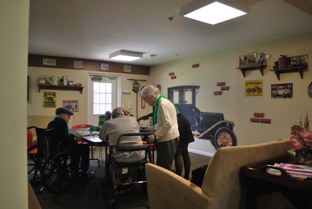 A group of elderly individuals engaged in an activity in a communal room decorated with vintage car images.