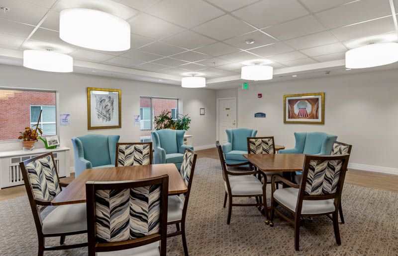 A modern lounge area with comfortable seating and tables, adorned with artwork and bright lighting.