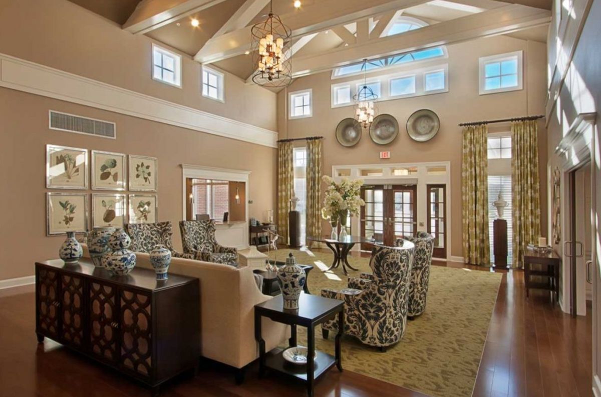 A spacious and elegantly designed living room with luxurious furniture and chandeliers, featuring a high ceiling and large windows.