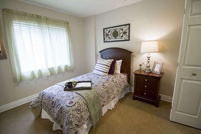 A cozy bedroom with a single bed and decorative pillows beside a nightstand and lamp.