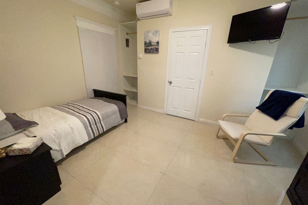 A minimalist bedroom with a single bed, chair, and wall-mounted TV.