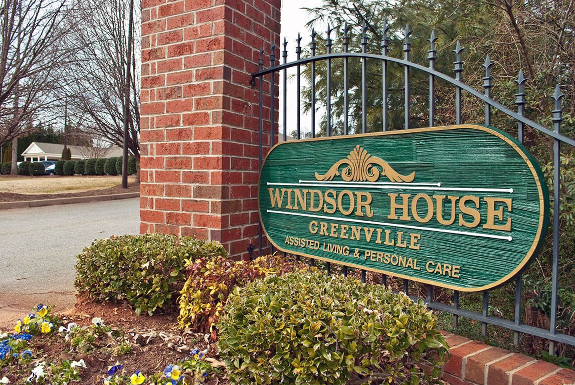 Entrance sign for Windsor House located in Greenville, featuring a brick structure and greenery.