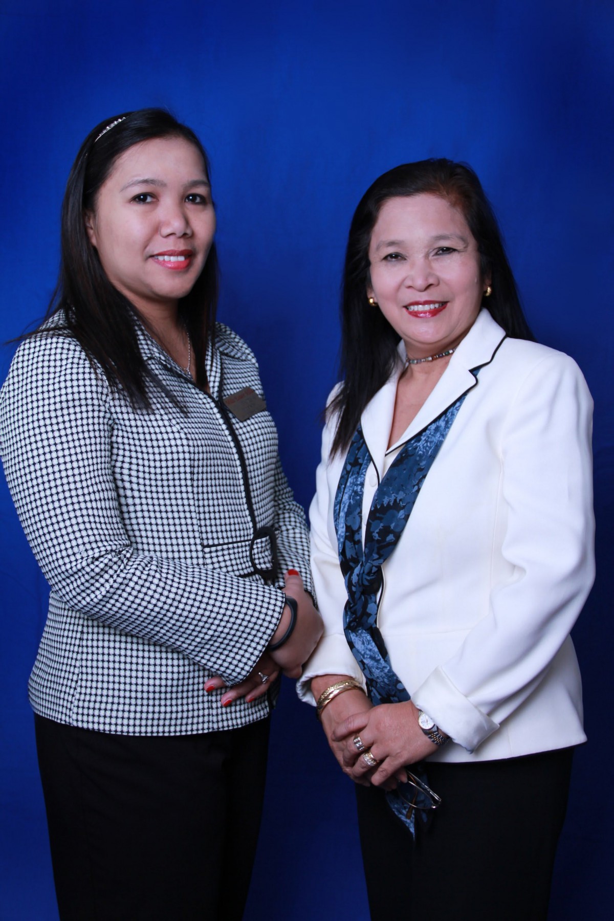 Two women posing together in formal attire with a blue background.