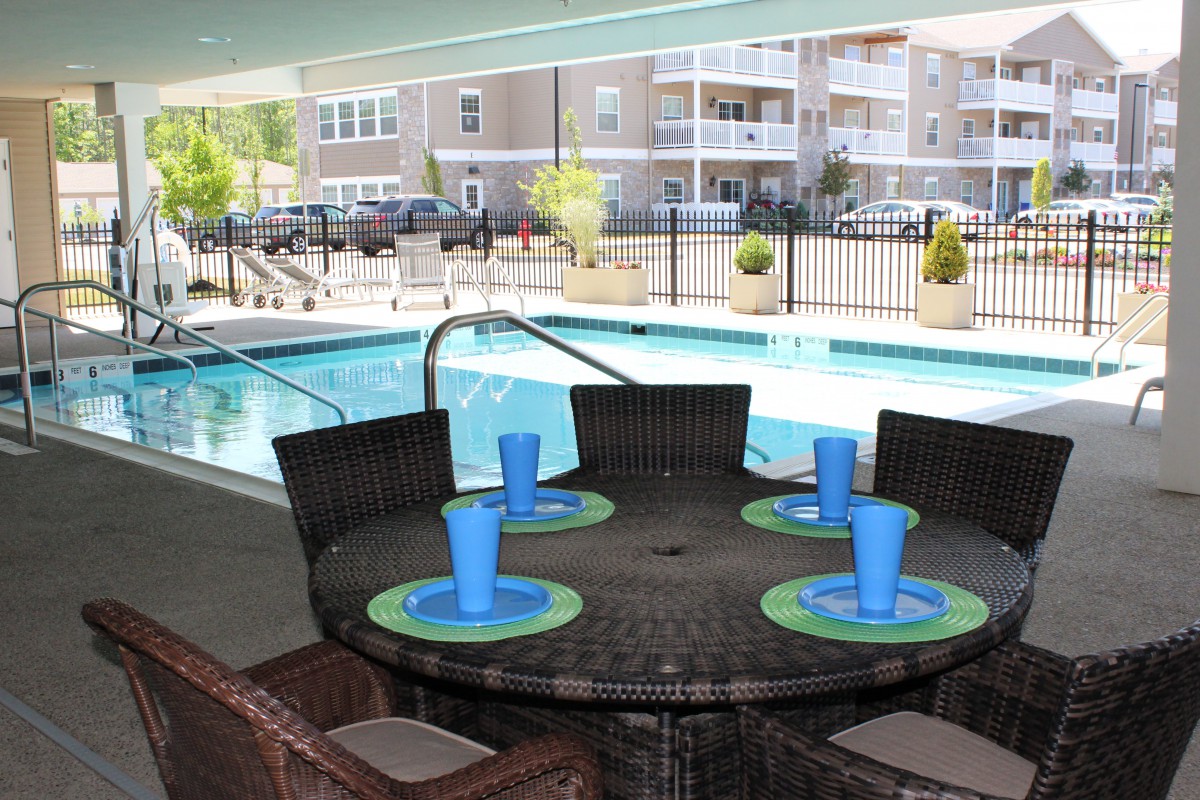An outdoor dining area with a table set near a swimming pool, surrounded by apartment buildings.