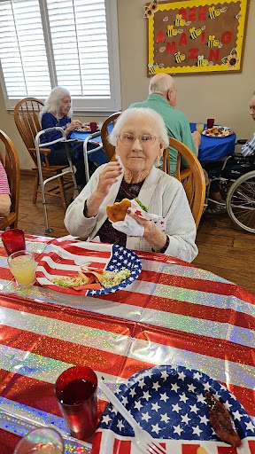 An elderly woman enjoys a meal during a community celebration, surrounded by festive decorations.