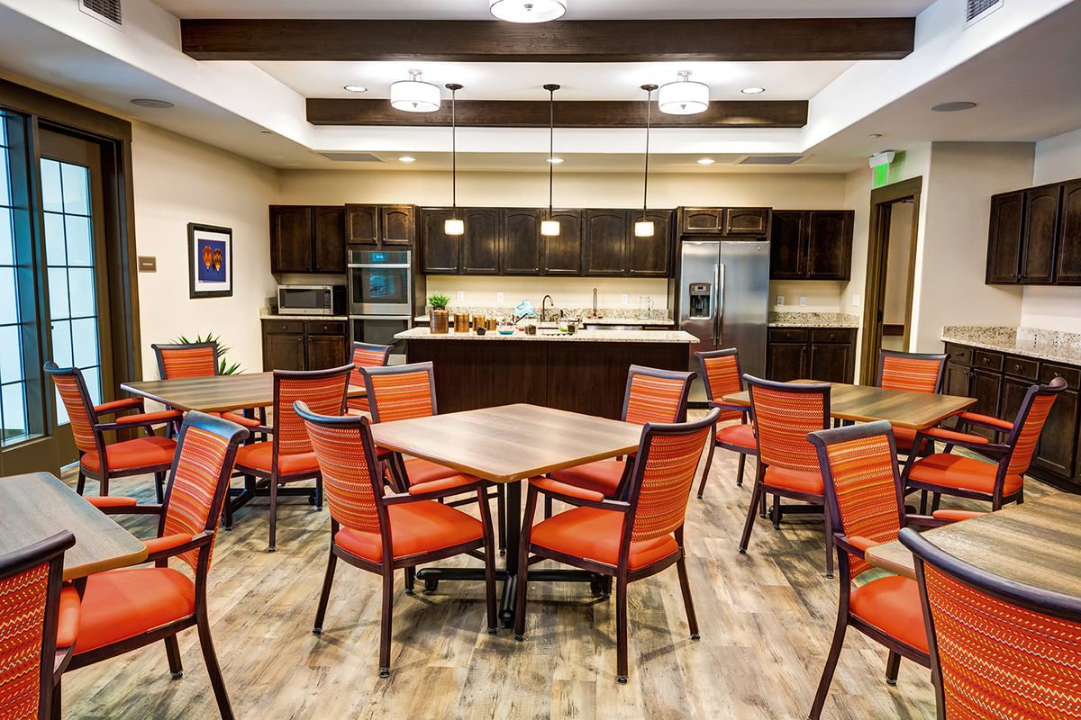 A modern dining and kitchen area with wooden tables, orange chairs, and stylish lighting.