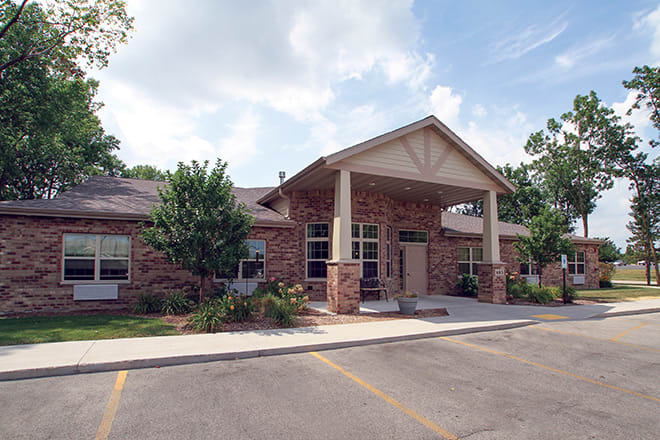A brick building with an entrance and surrounding greenery under a partly cloudy sky.