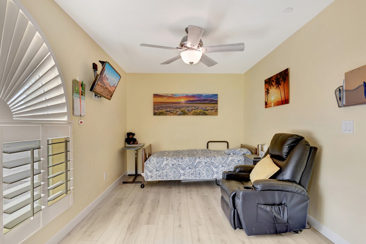 A cozy bedroom with a bed, recliner, wall-mounted TV, and ceiling fan.
