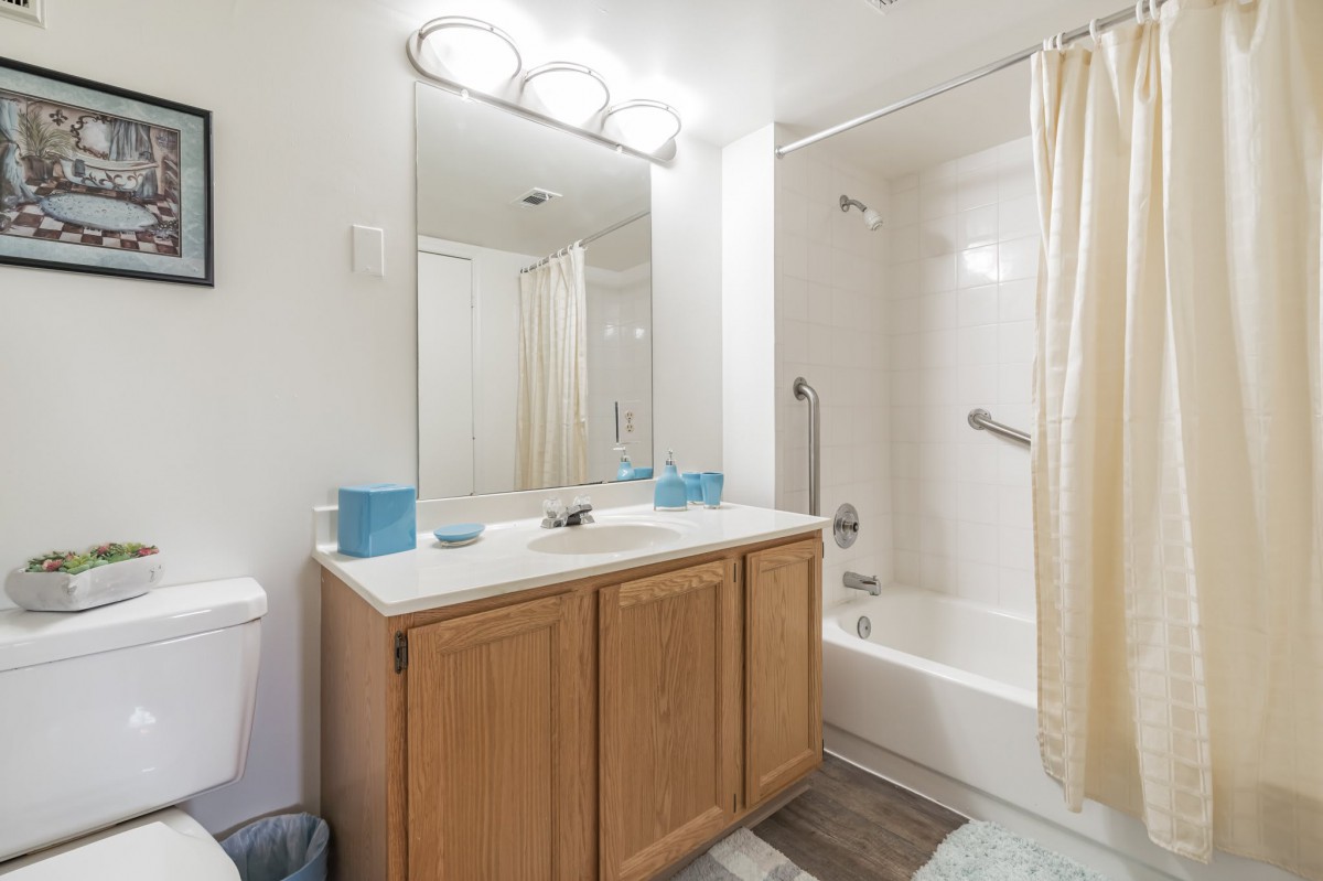 A modern bathroom with a wooden vanity, large mirror, and bathtub with a shower curtain.