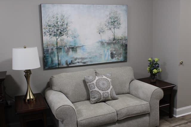 A cozy living room with a gray sofa, decorative cushion, and a serene landscape painting on the wall.