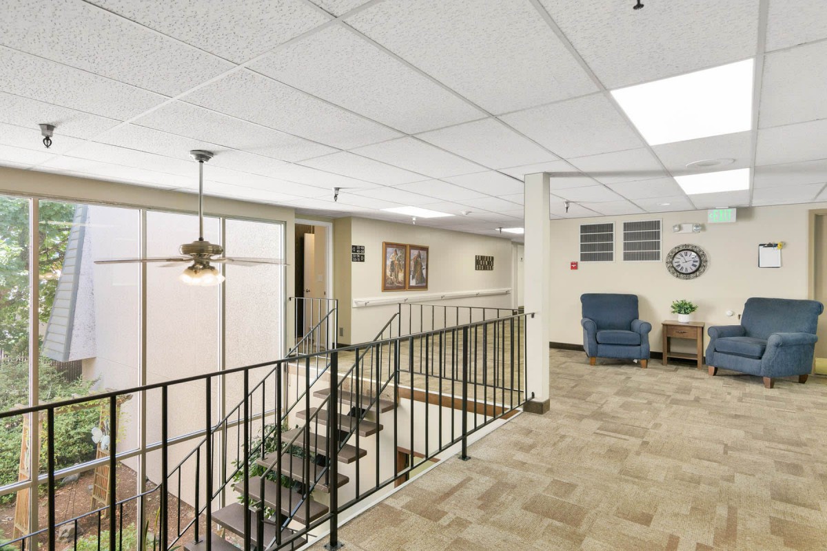 A well-lit office hallway featuring a staircase with black railings and comfortable seating.