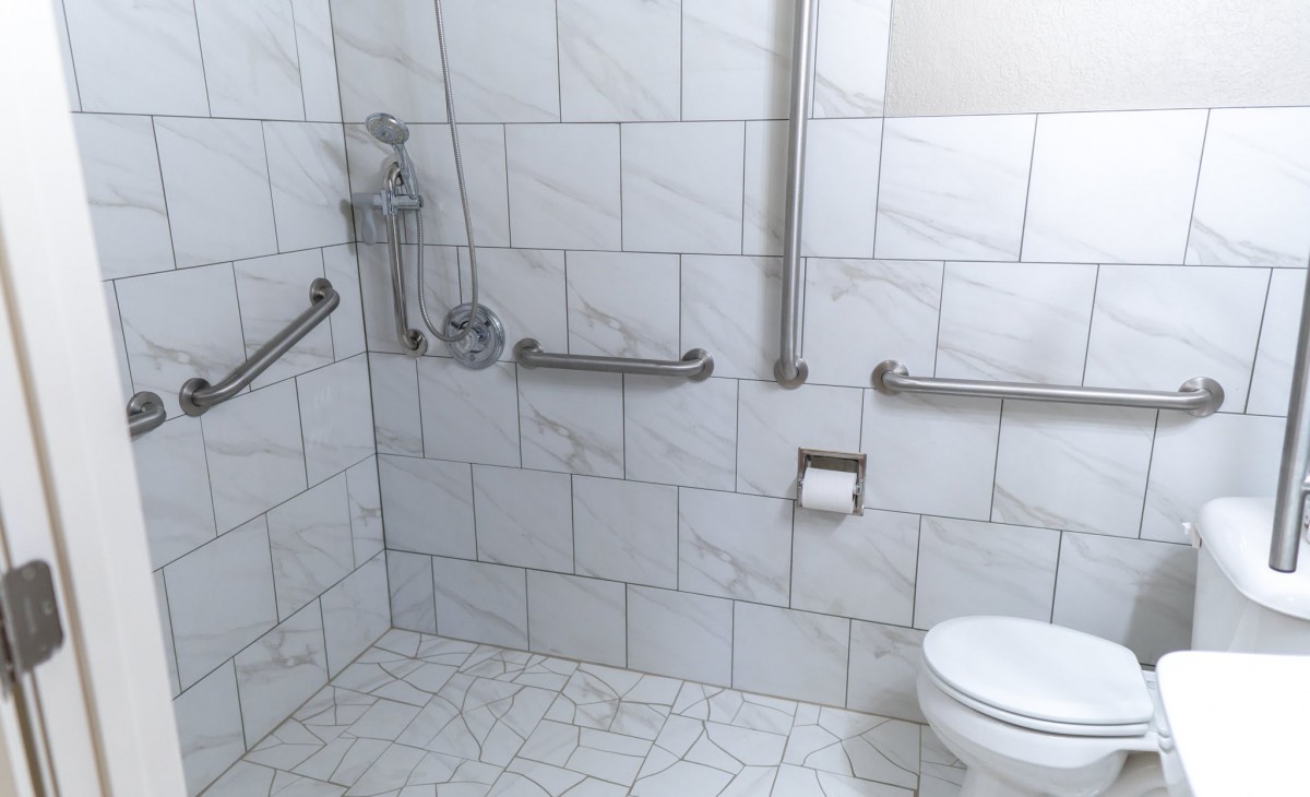 An accessible bathroom featuring grab bars and a tiled interior.