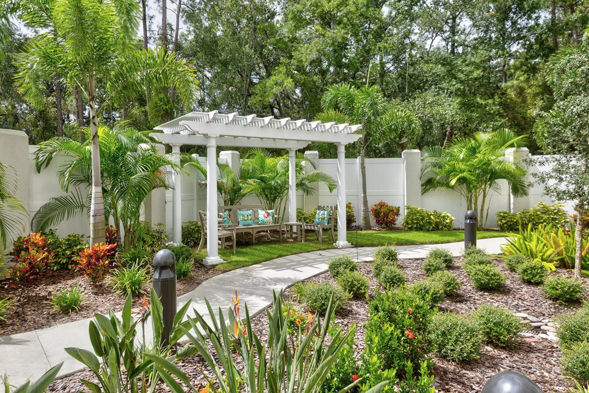 A beautifully landscaped garden featuring a white pergola surrounded by lush greenery and a winding pathway.