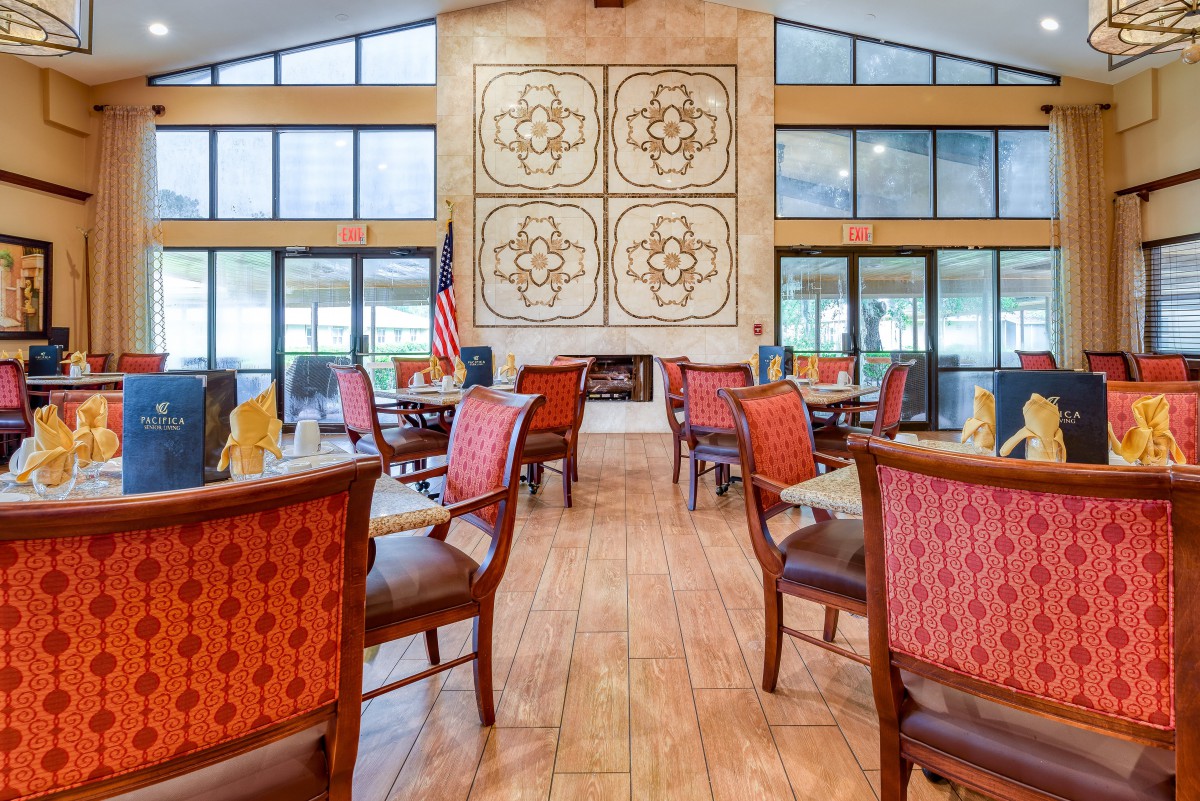 A well-lit dining area with red cushioned chairs, tables set for service, and large decorative wall art.