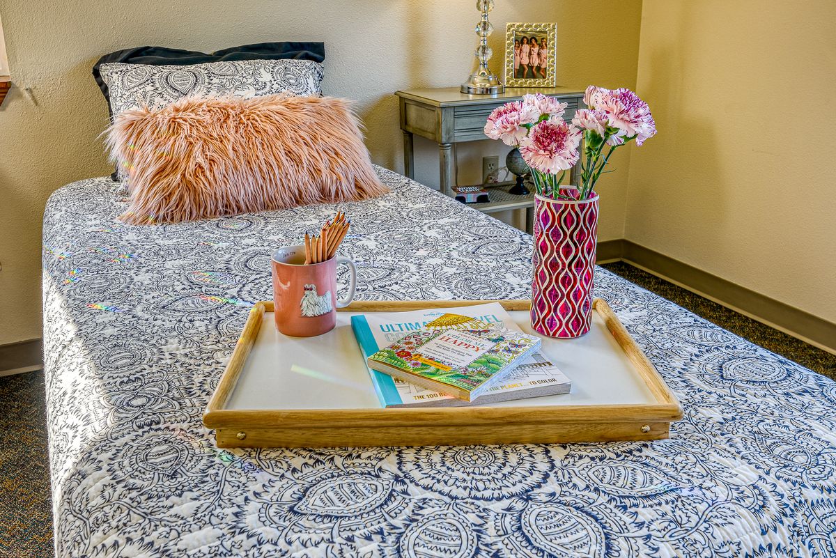A cozy bedroom setup with a stylish tray on the bed, featuring flowers in a vase, books, and a soft pillow.