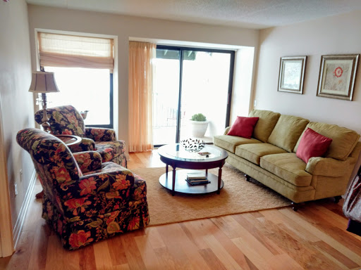 A cozy living room featuring a green sofa, floral armchairs, and a round coffee table, illuminated by natural light from the window.