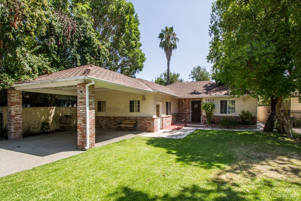 A charming single-story house with a well-maintained front yard and tall trees.