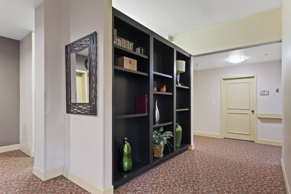 A hallway with a large black bookshelf filled with decorative items and a mirror on the wall.
