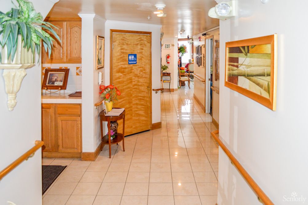 A well-decorated hallway with tile flooring, featuring a wooden door and decorative elements such as plants and paintings.
