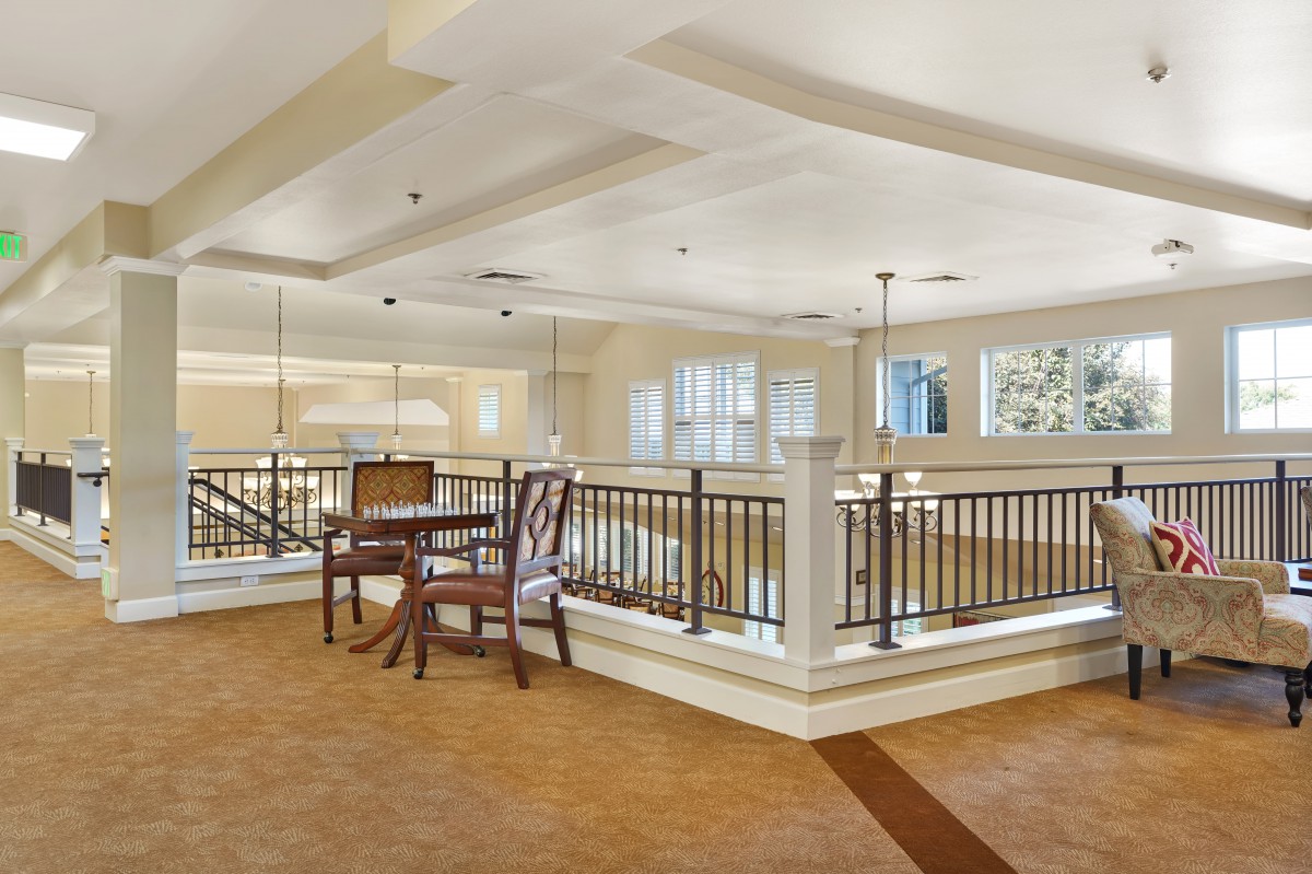 A cozy dining area with wooden furniture and ceiling lights, featuring a carpeted floor and decorative railings.